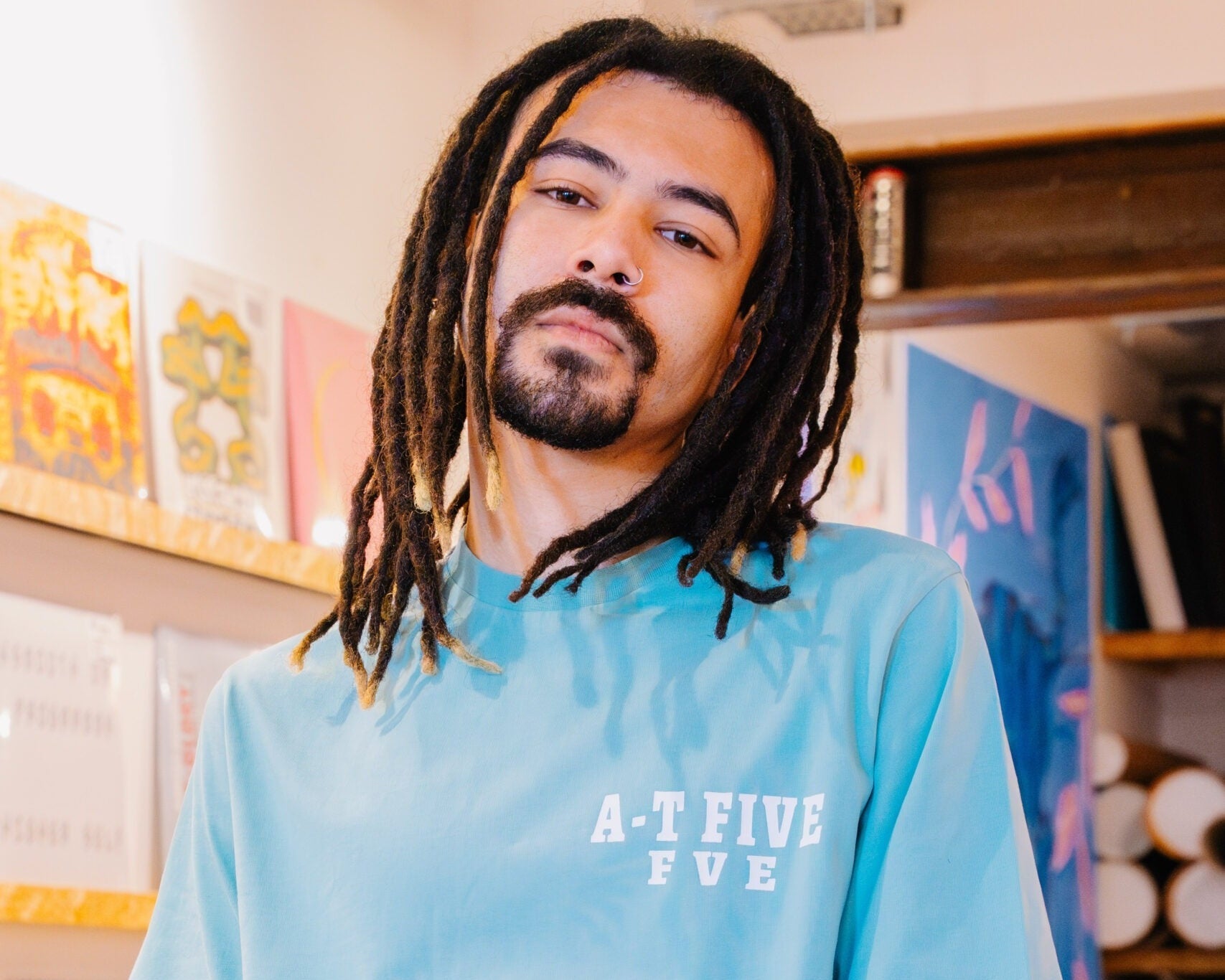 Man wearing a light blue t-shirt with 'A-T Five' text in a casual setting.
